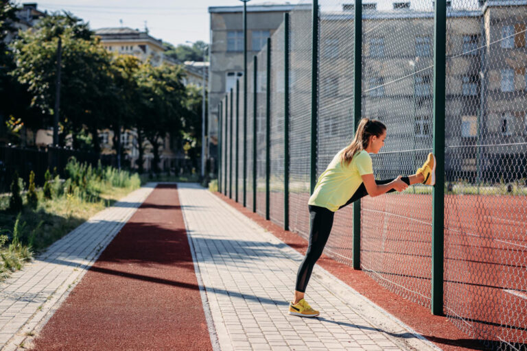 Imagem mulher fazendo alongamento próximo a cerca de arame em quadra esportiva