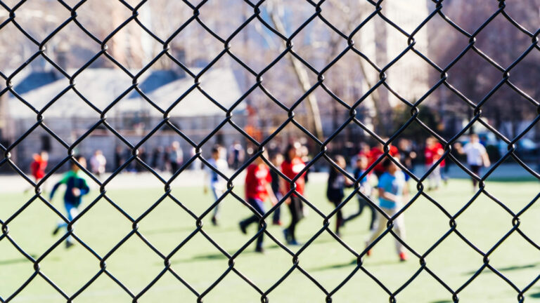 imagem de grade de proteção com alunos ao fundo ofuscados